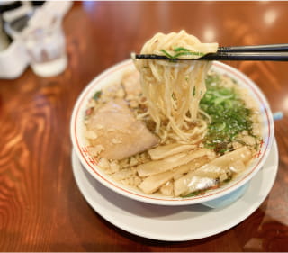 写真:ラーメンの器から箸で麺を持ち上げている
